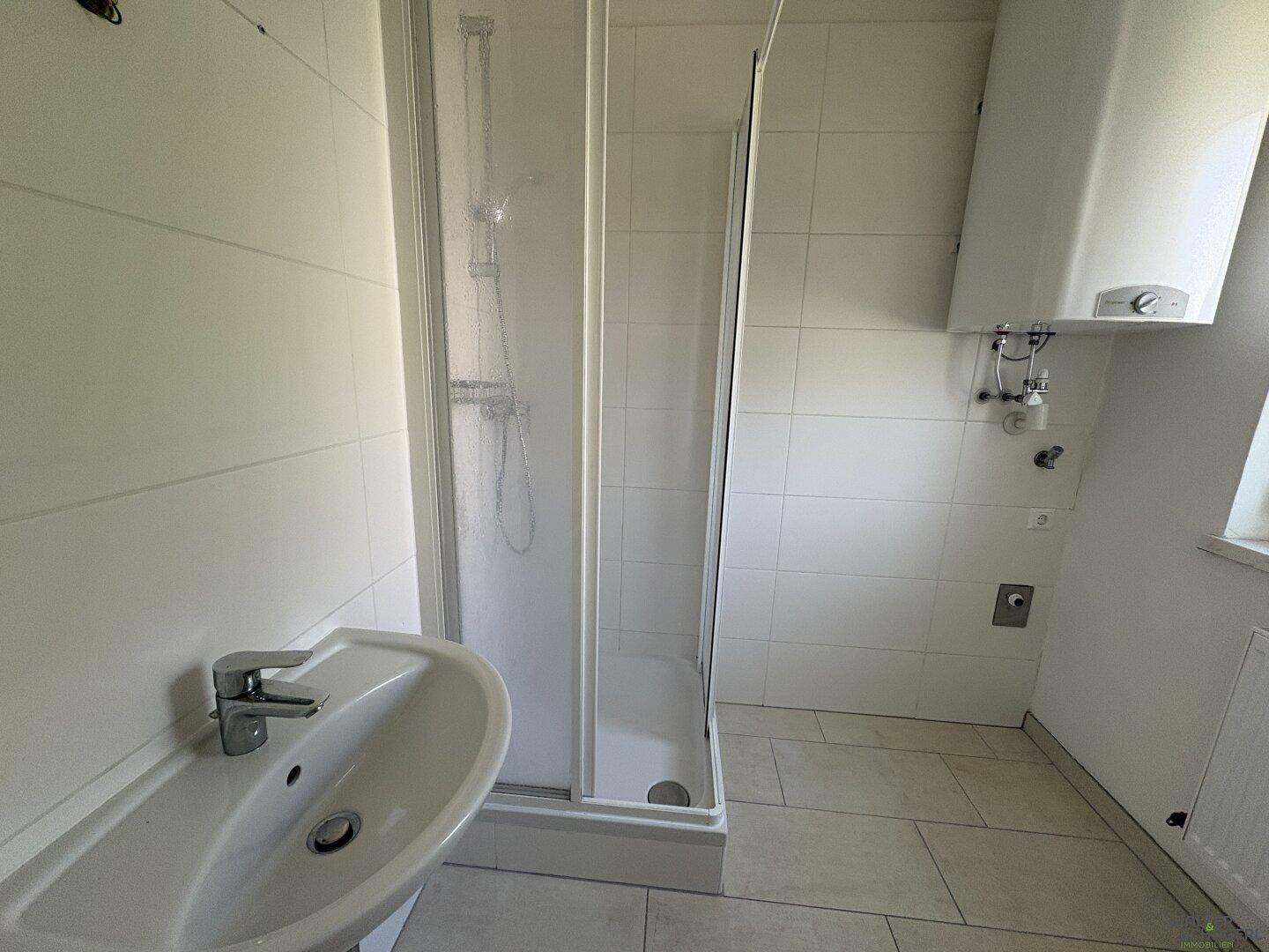 Funktionales Badezimmer mit Duschkabine, Waschbecken und Wandheizung.