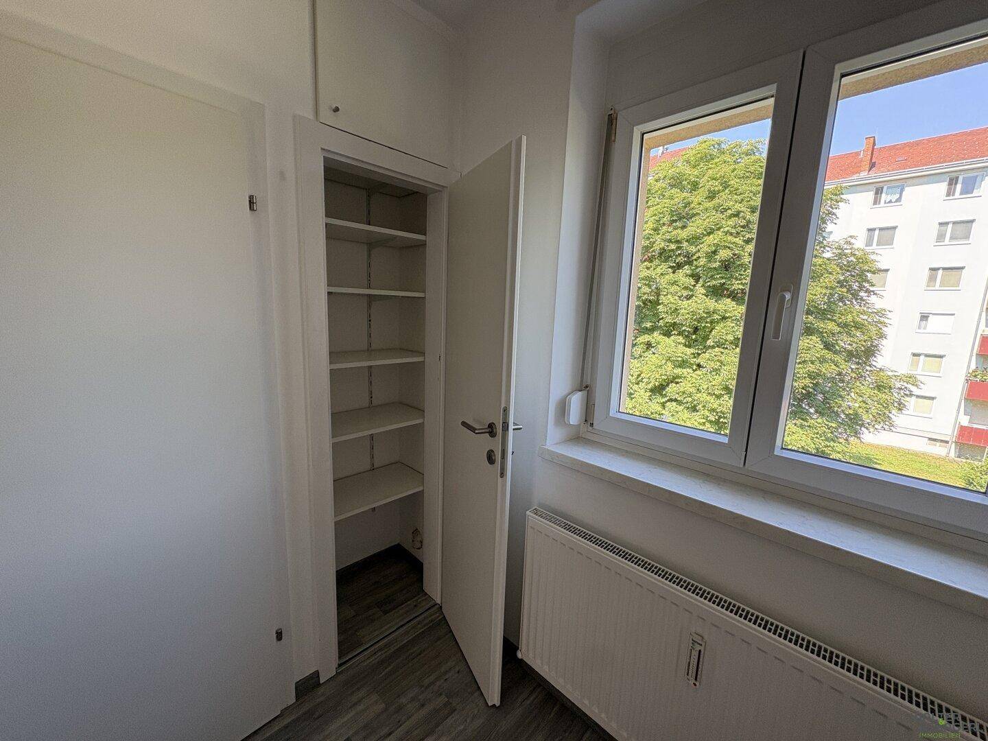 Heller Raum mit Fenster, Heizkörper und praktischem Einbauschrank mit Regalen.