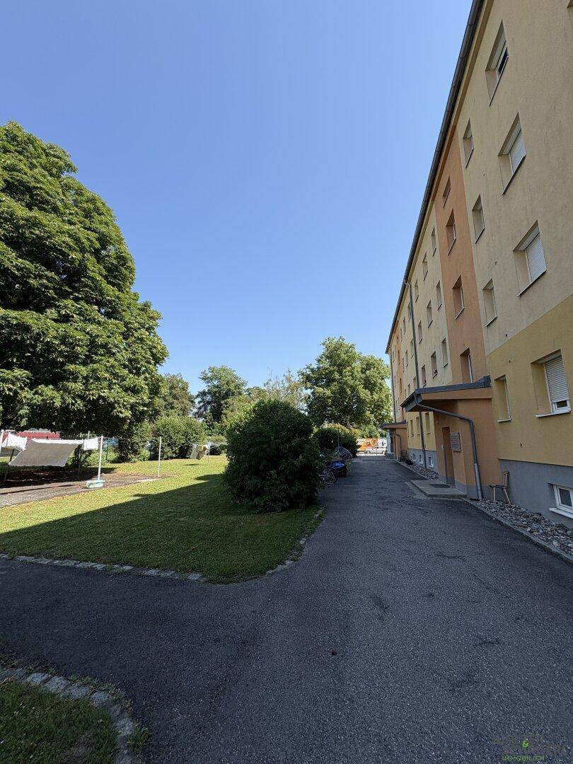 Mehrfamilienhaus mit gepflegter Grünfläche, Bäumen und einem Gehweg im Außenbereich.