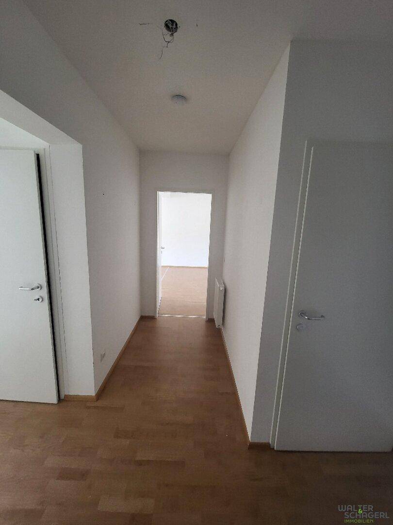 Heller Flur mit hellem Holzfußboden und weißen Wänden, der zu weiteren Räumen führt.