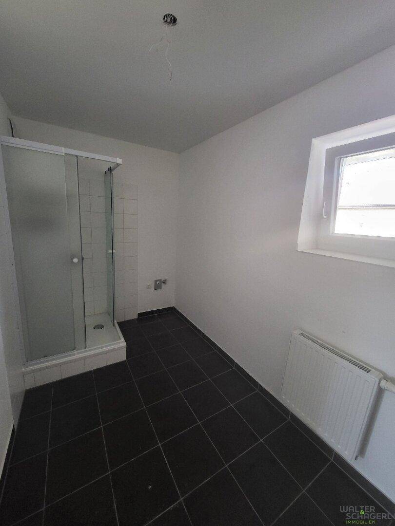 Modernes Badezimmer mit dunklen Fliesen, Duschkabine, Fenster und Heizkörper.