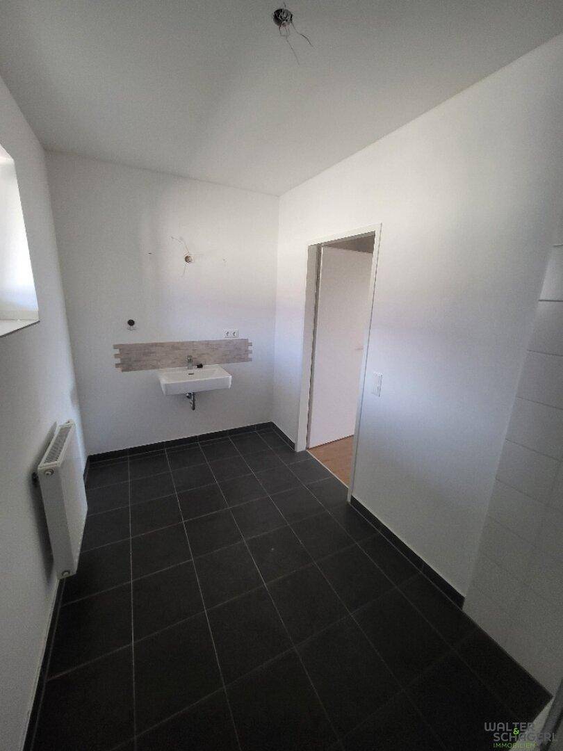Helles Badezimmer mit dunklem Fliesenboden, Fenster und vorbereiteter Waschtischinstallation.