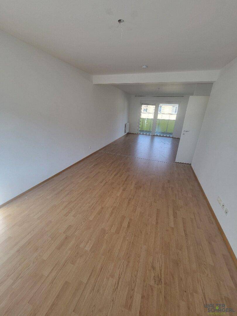 Geräumiges, helles Wohnzimmer mit Holzfußboden und Zugang zu einem Balkon.