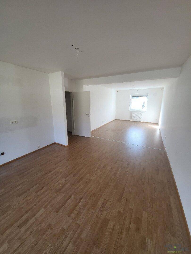 Offener Wohnbereich mit hellem Holzfußboden, weißen Wänden und viel Tageslicht.