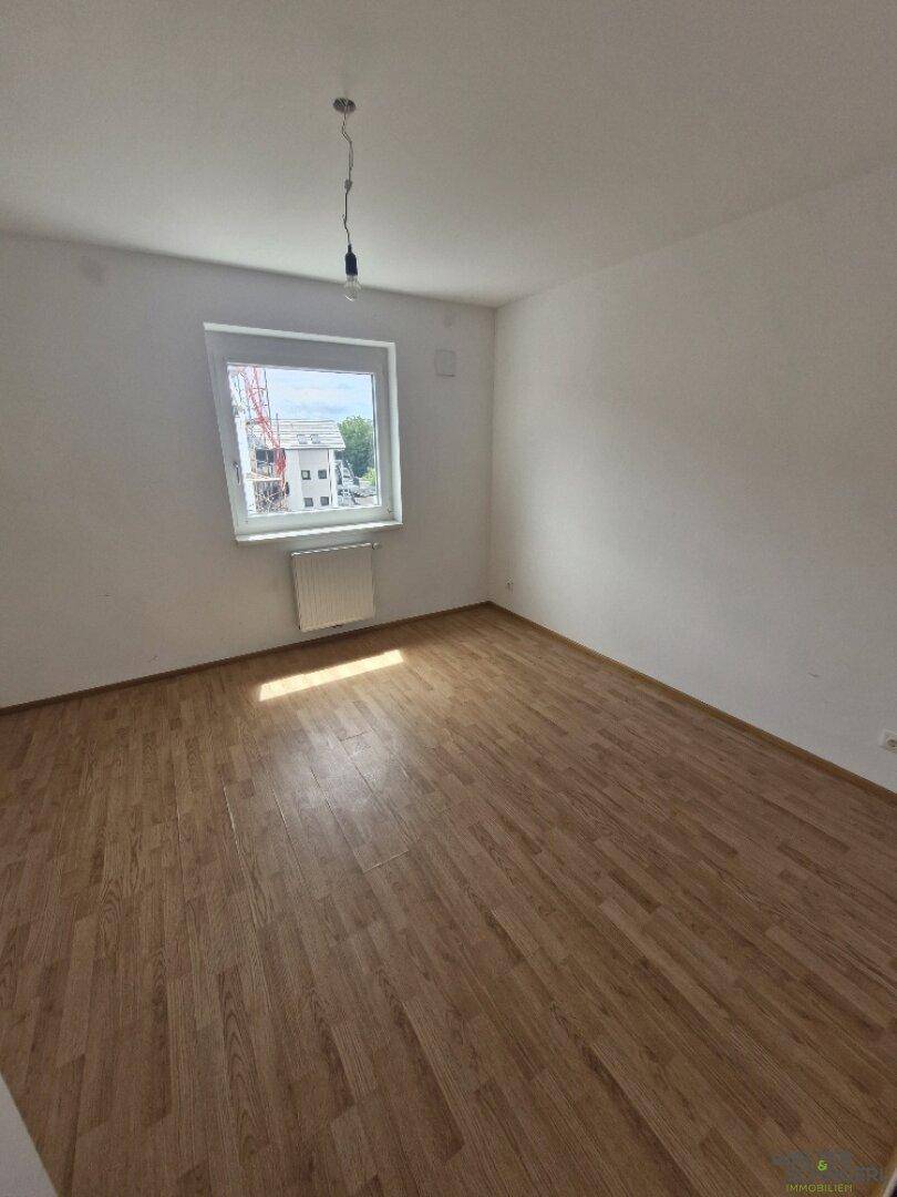 Leeres Zimmer mit Laminatboden, weiß gestrichenen Wänden und Fenster mit Stadtblick.