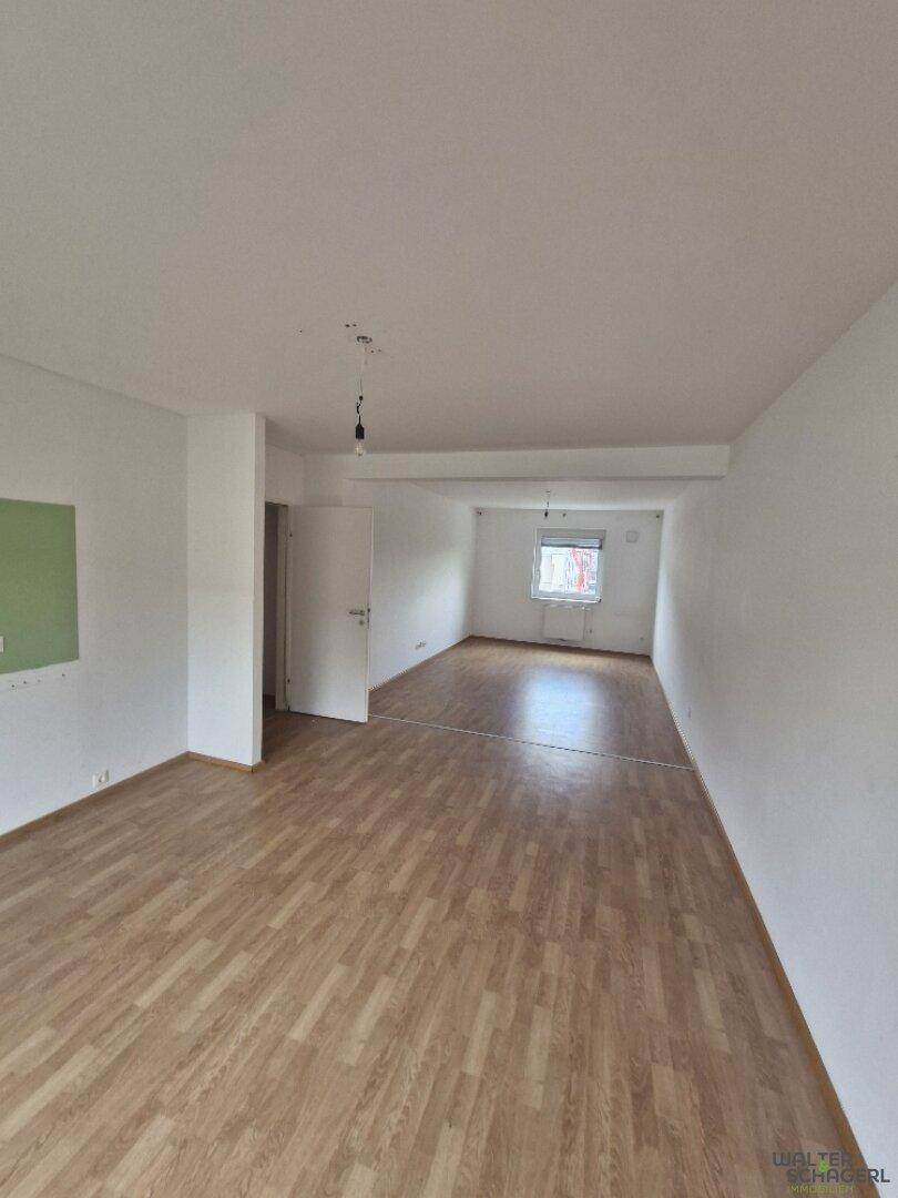 Geräumiges, leeres Wohnzimmer mit Laminatboden und viel Tageslicht durch das Fenster.