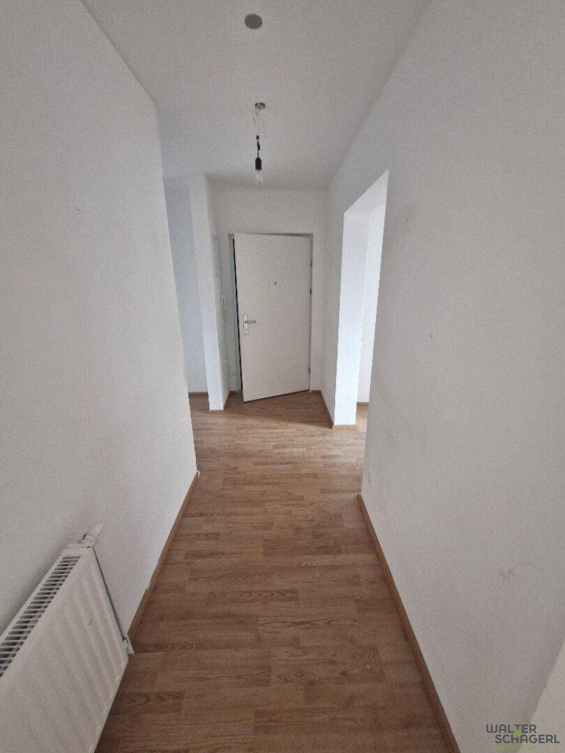 Langer, heller Flur mit Laminatboden und weiß gestrichenen Wänden, führt zu weiteren Räumen.