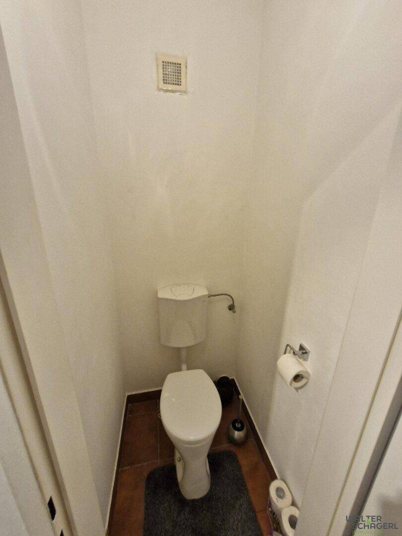 Kleines Gäste-WC mit Toilette und Abluftsystem, funktional und platzsparend gestaltet.