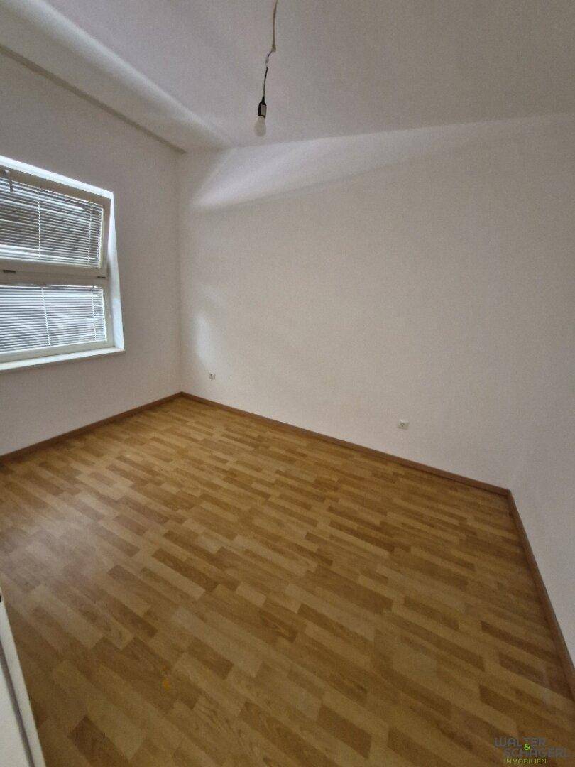 Leeres Schlafzimmer mit Holzfußboden und einem Fenster mit Jalousien, bereit zur individuellen Gestaltung.