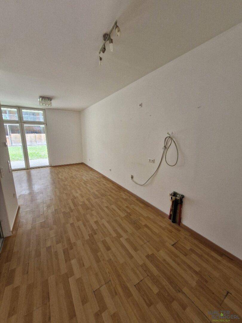 Geräumiges Wohnzimmer mit Holzfußboden und großen Glastüren, die Zugang zum Außenbereich bieten.