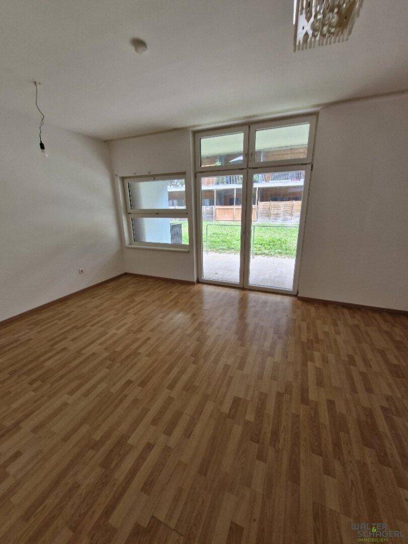 Helles Zimmer mit Holzfußboden und großen Fenstern, die viel Tageslicht hereinlassen und einen Zugang bieten.