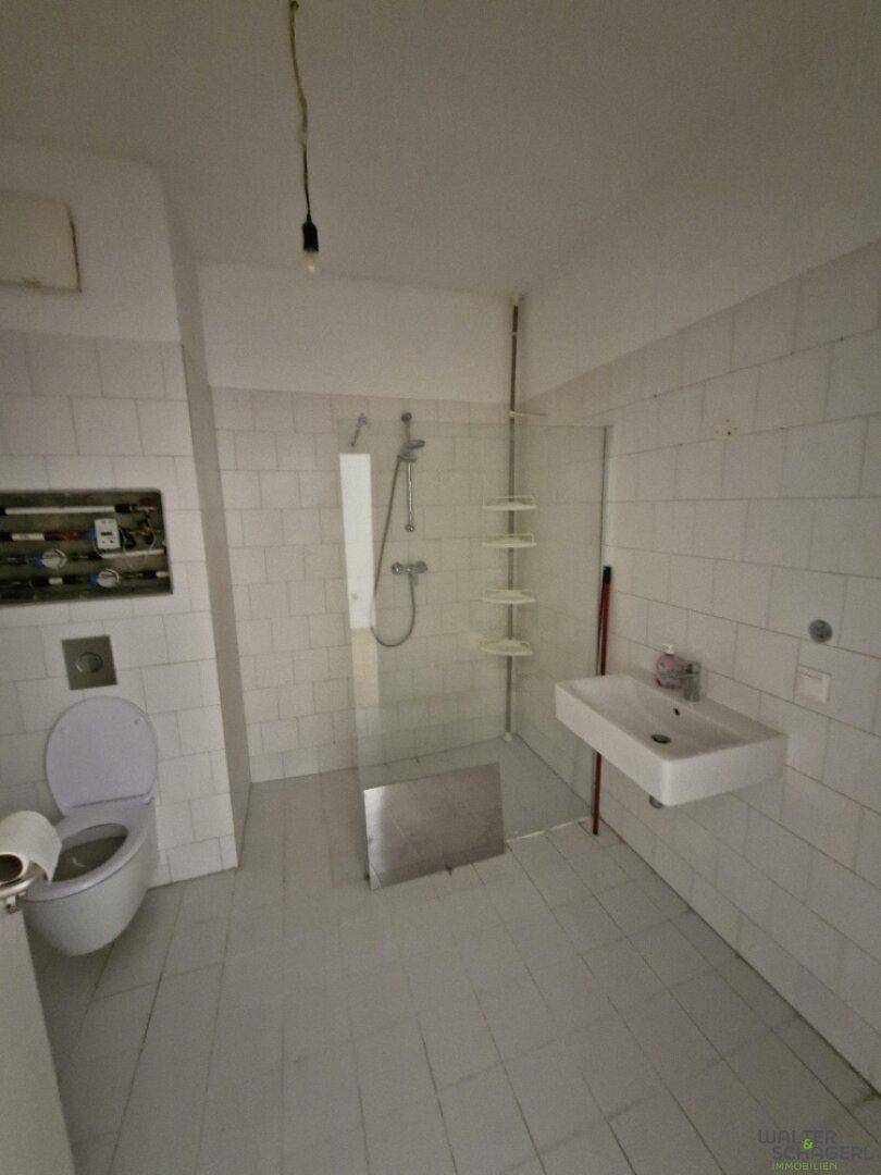 Modernes Badezimmer mit weißen Fliesen, Dusche, Toilette und Waschbecken, in gutem Zustand.
