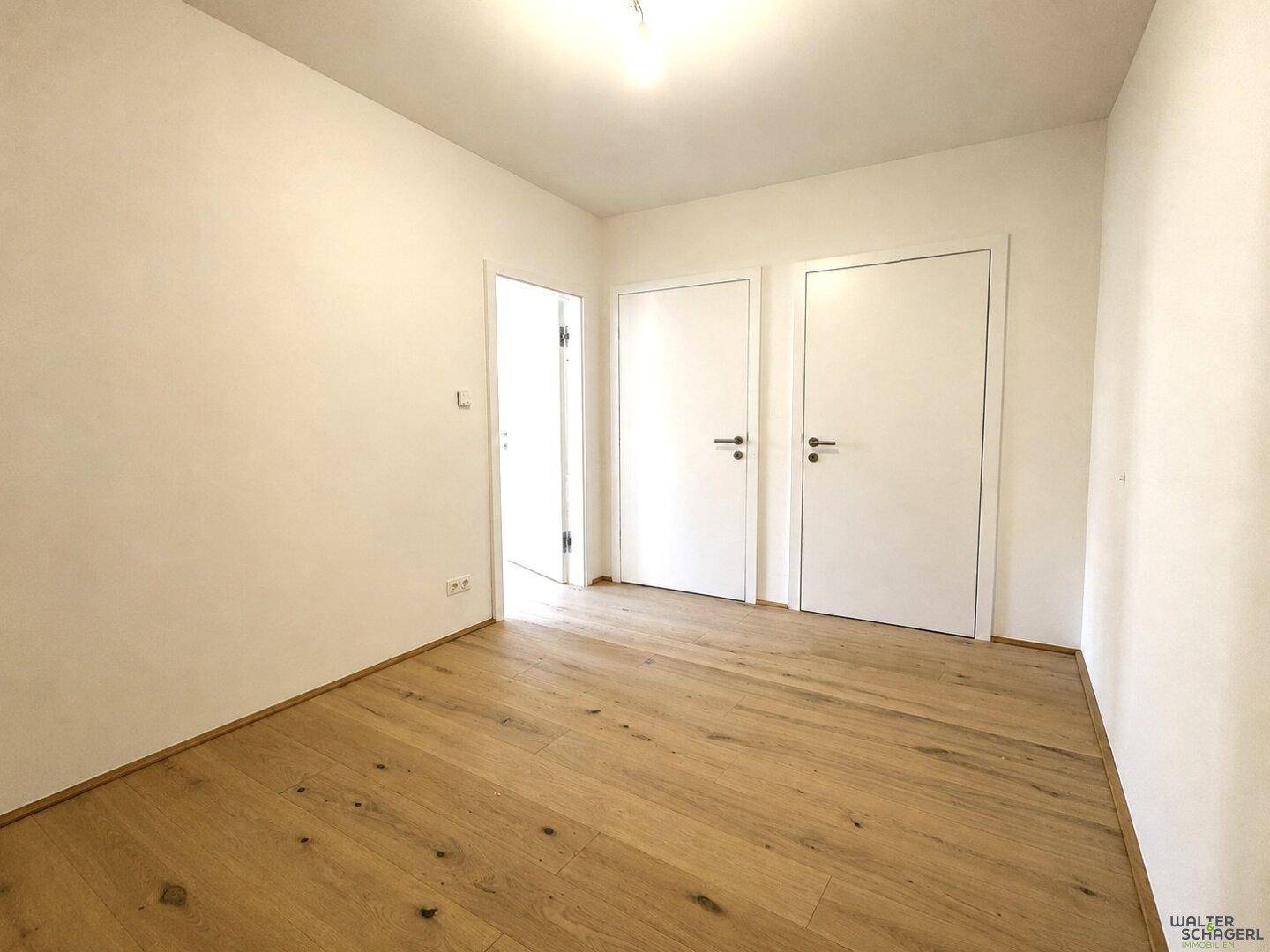 Leerer Raum mit hellem Holzfußboden und weißen Wänden, bereit zur individuellen Gestaltung.