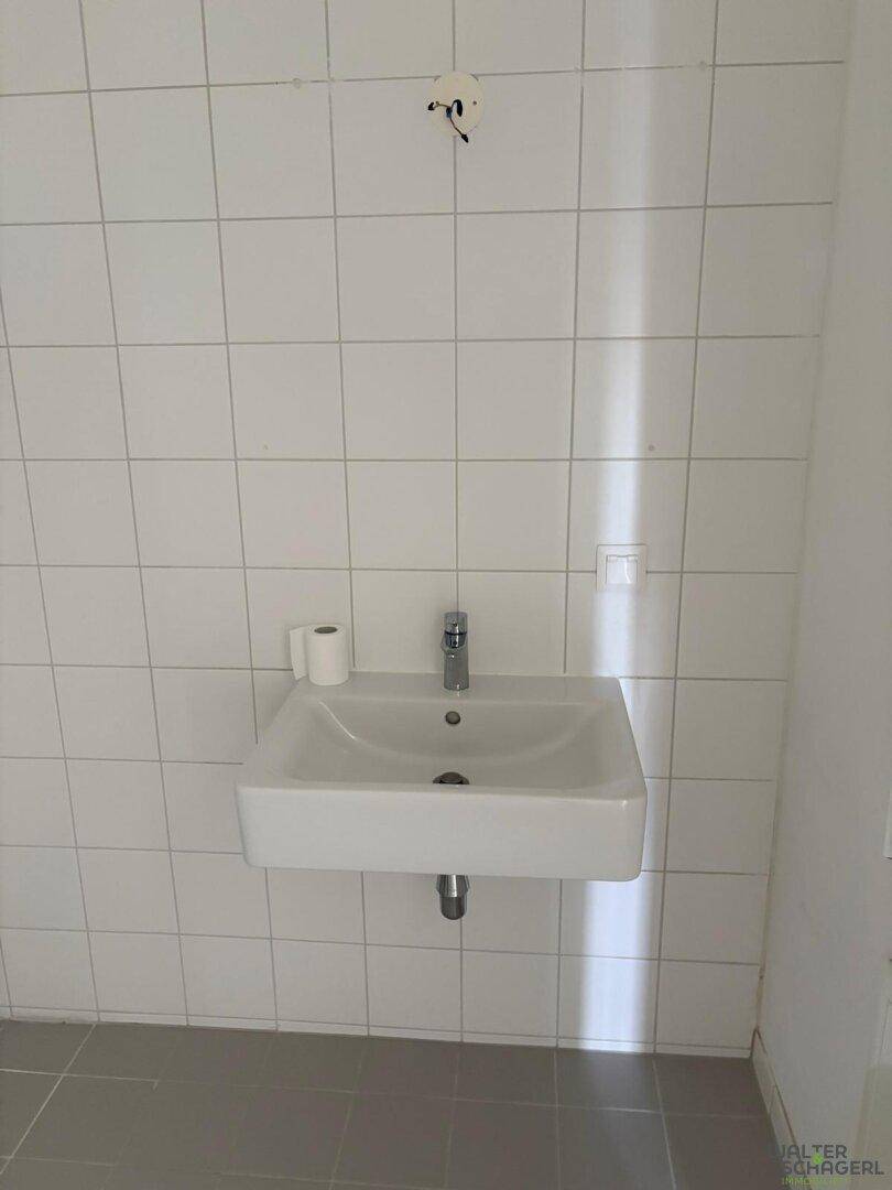 Modernes Badezimmer mit weißen Fliesen und einem einzelnen Waschbecken an der Wand.