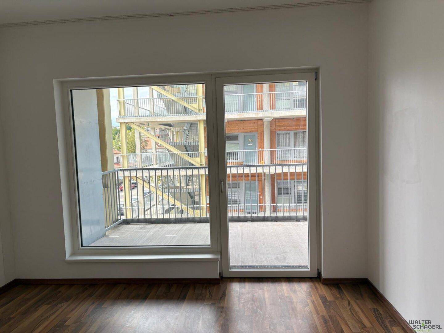 Heller Innenraum mit Laminatboden und Zugang zu einem Balkon mit Blick auf die Umgebung.