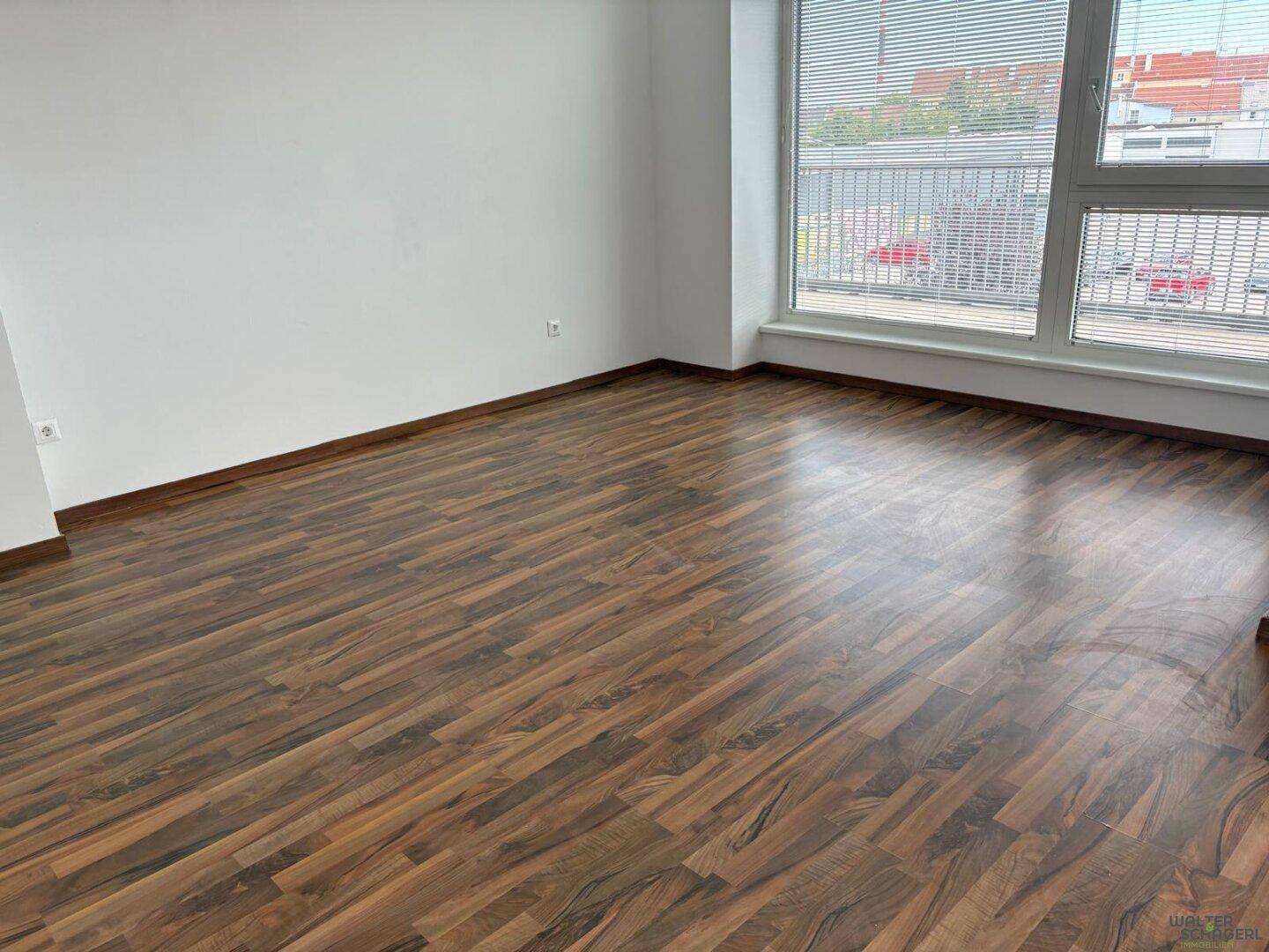 Geräumiger, heller Raum mit Laminatboden und großen Fenstern, die viel Tageslicht hereinlassen.
