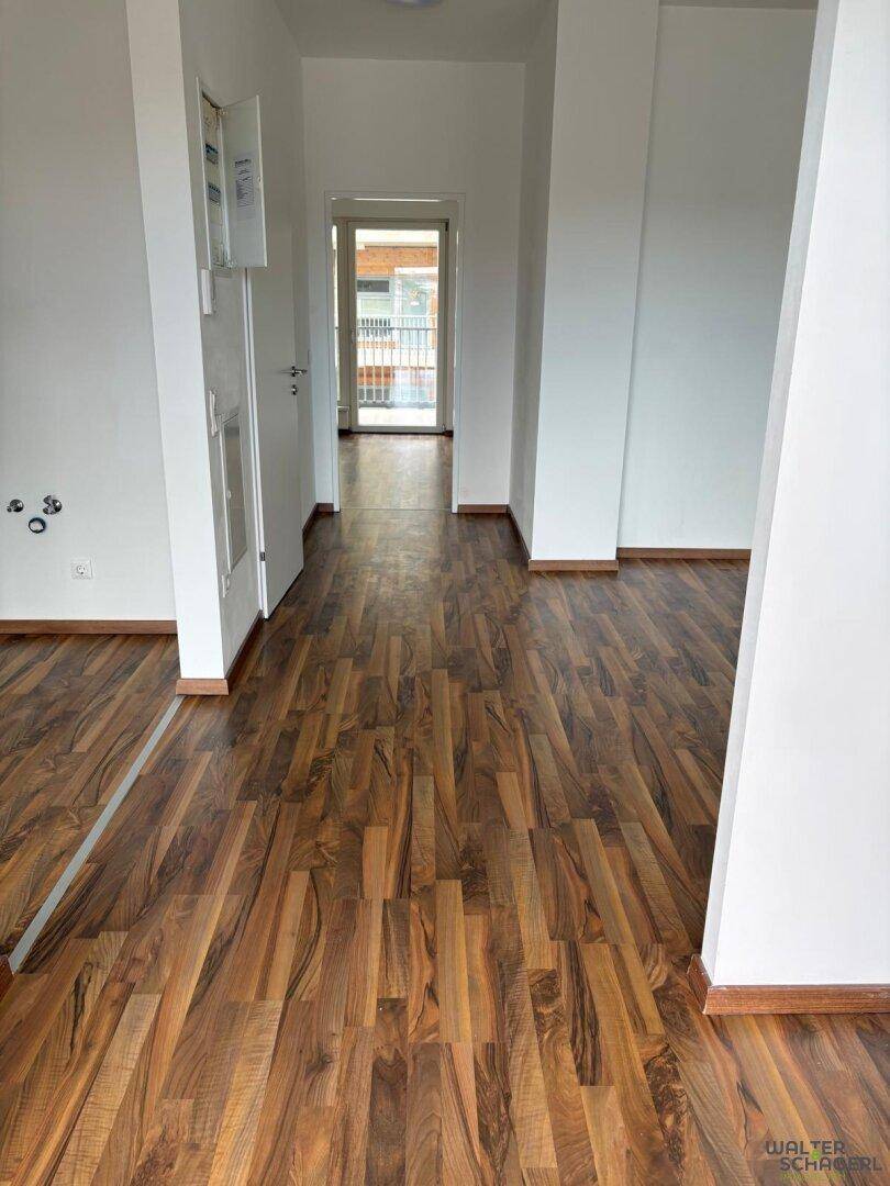 Heller Flur mit Laminatboden, der zu einem weiteren Raum mit Balkonzugang führt.