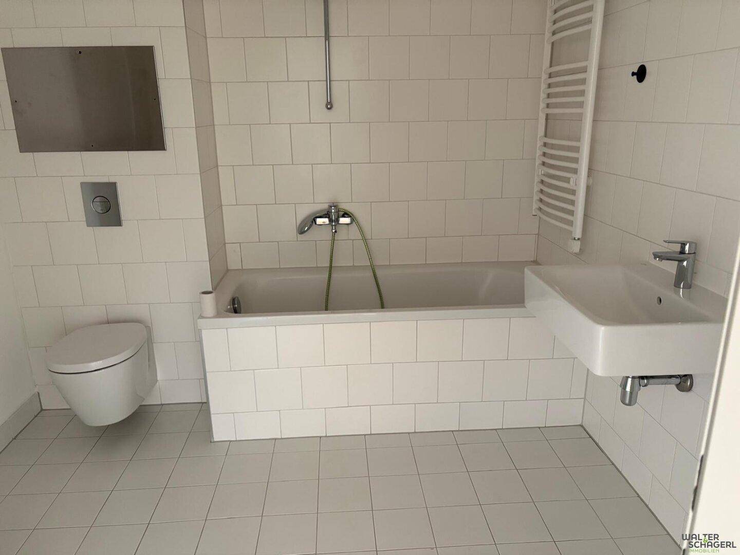 Helles Badezimmer mit weißen Fliesen, Badewanne, WC und Handtuchheizkörper.
