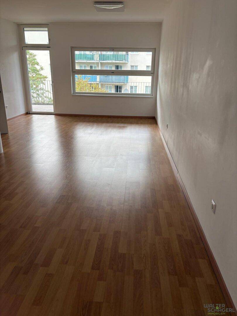 Leerer Raum mit Laminatboden, großen Fenstern und Zugang zu einem Außenbereich.