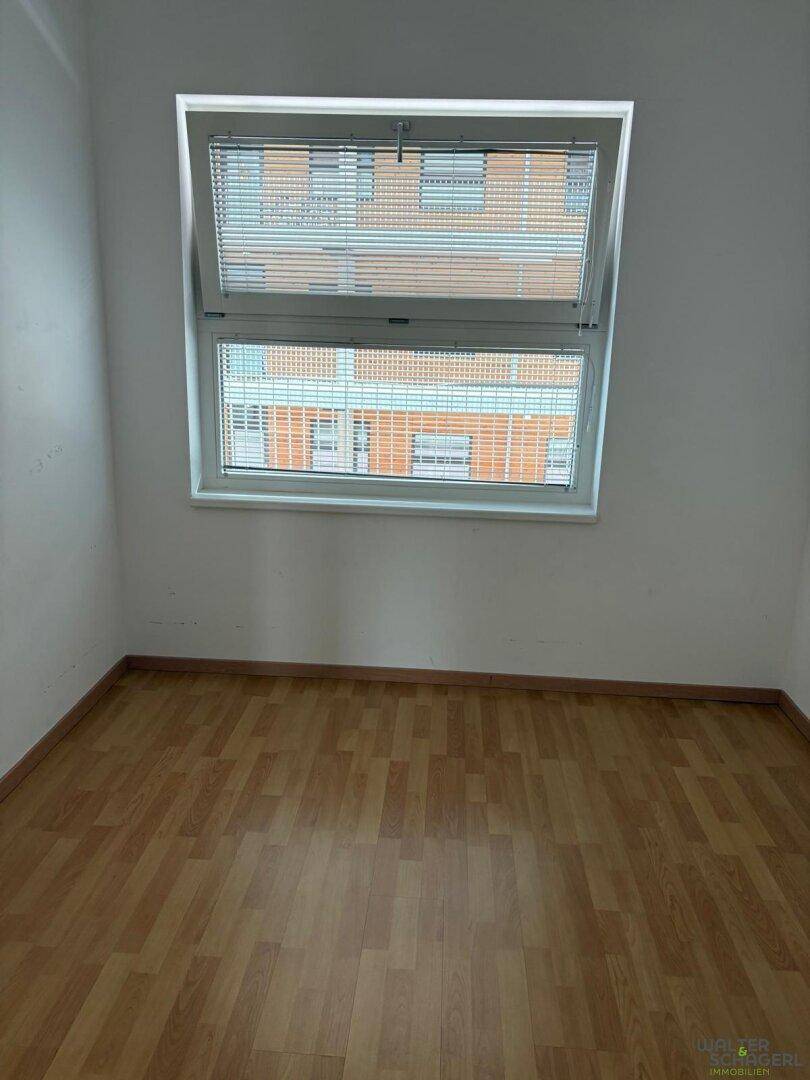 Unmöblierter Raum mit Laminatboden und Fenster mit Jalousien für Privatsphäre.