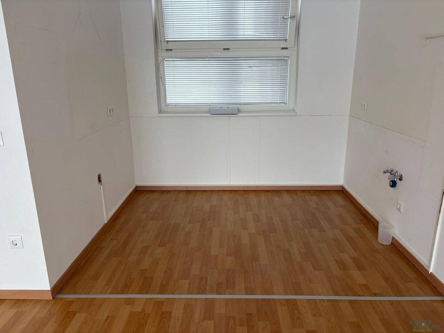 Leerer Raum mit Laminatboden und Anschlüssen für eine mögliche Küchen- oder Waschküchennutzung.