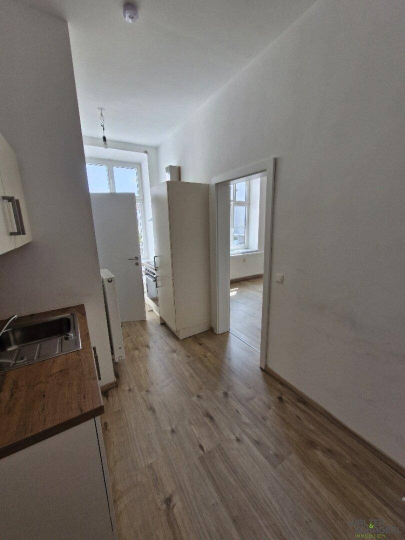 Kleine Küche mit Holz-Arbeitsplatte und Laminatboden, offen zu einem weiteren Raum.