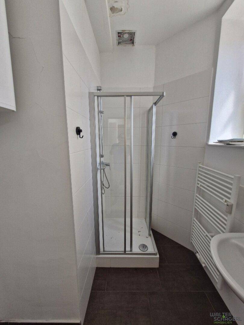 Helles Badezimmer mit Duschkabine, weißen Fliesen und beheiztem Handtuchhalter.