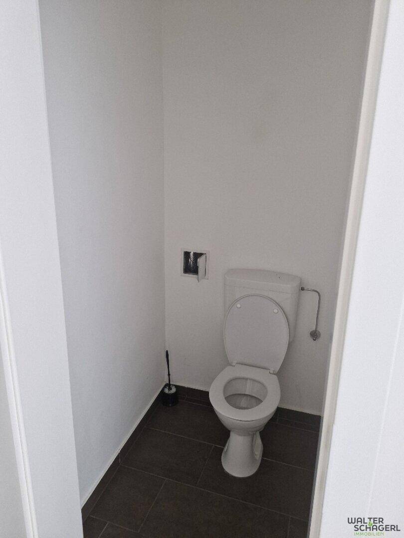Separates WC mit Toilette und dunklen Bodenfliesen in einem schlichten Design.
