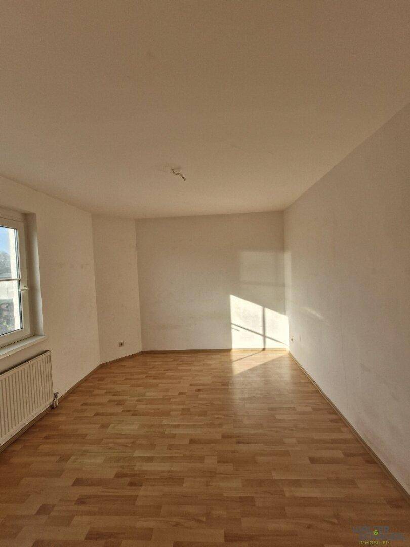 Helles Schlafzimmer mit Holzboden, weißen Wänden und einem Fenster, das Sonnenlicht hereinlässt.