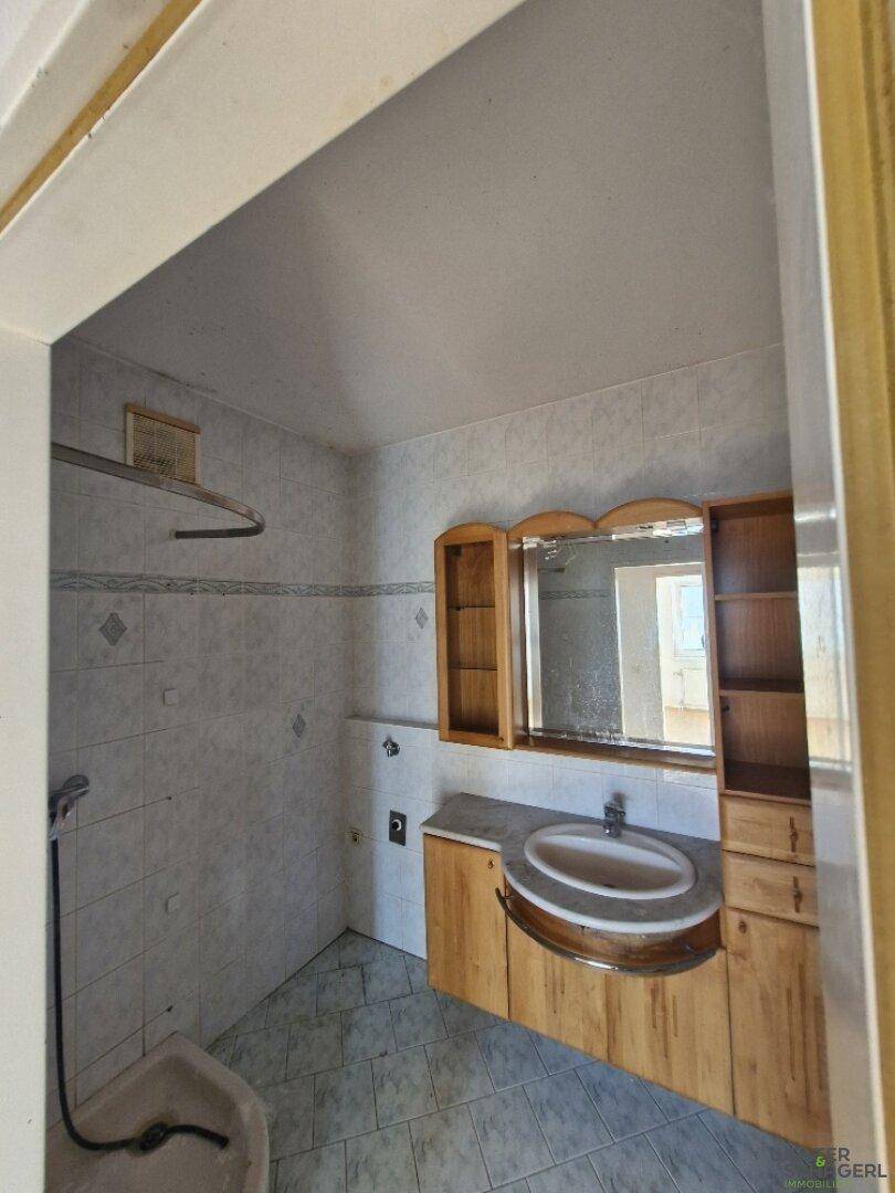 Badezimmer mit hellen Fliesen, Holzwaschtisch und Spiegelschrank, ausgestattet mit einer Dusche.