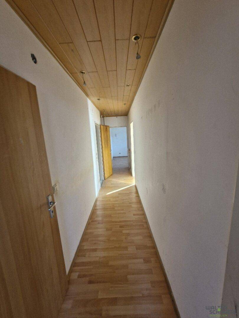 Langer Flur mit Holzboden, weißen Wänden und einer Holzdeckenverkleidung, der zu weiteren Räumen führt.