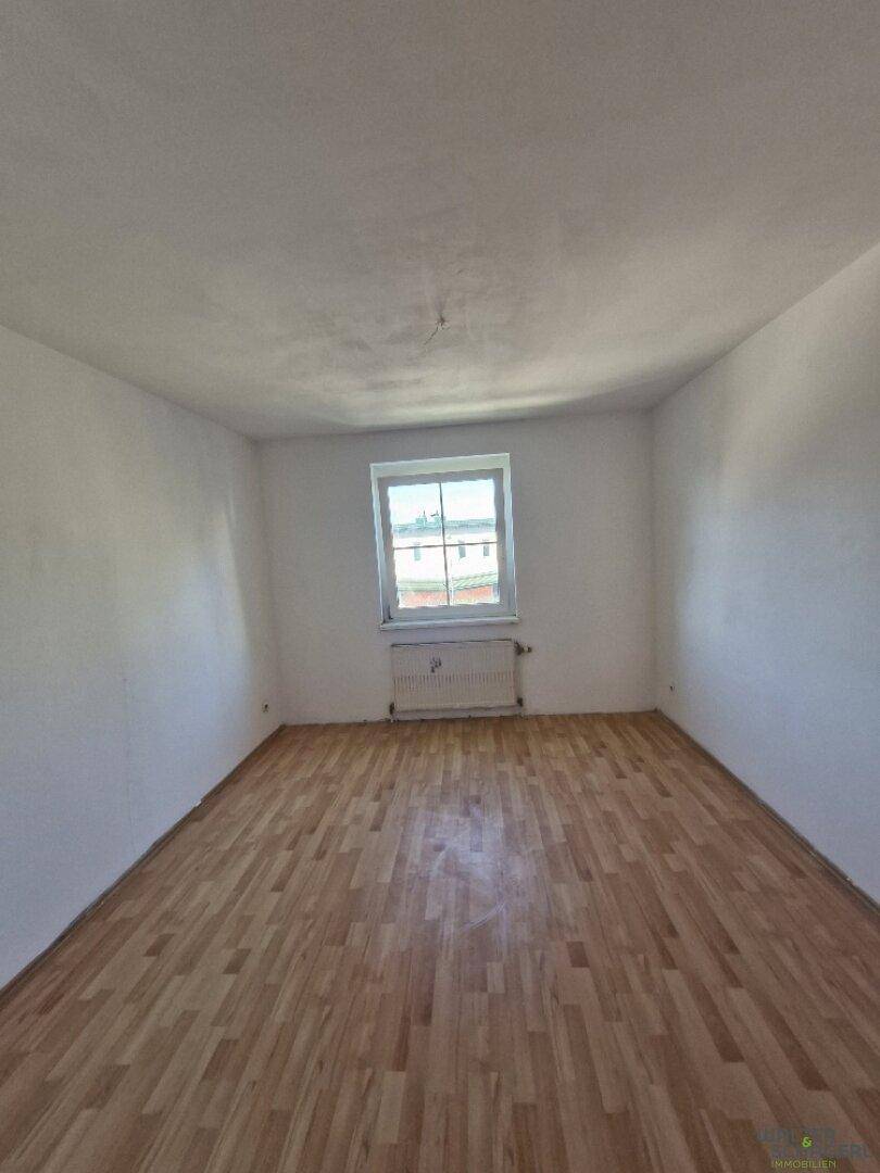 Leeres Zimmer mit Holzboden, weißen Wänden und einem Fenster, ideal als Schlaf- oder Arbeitszimmer.