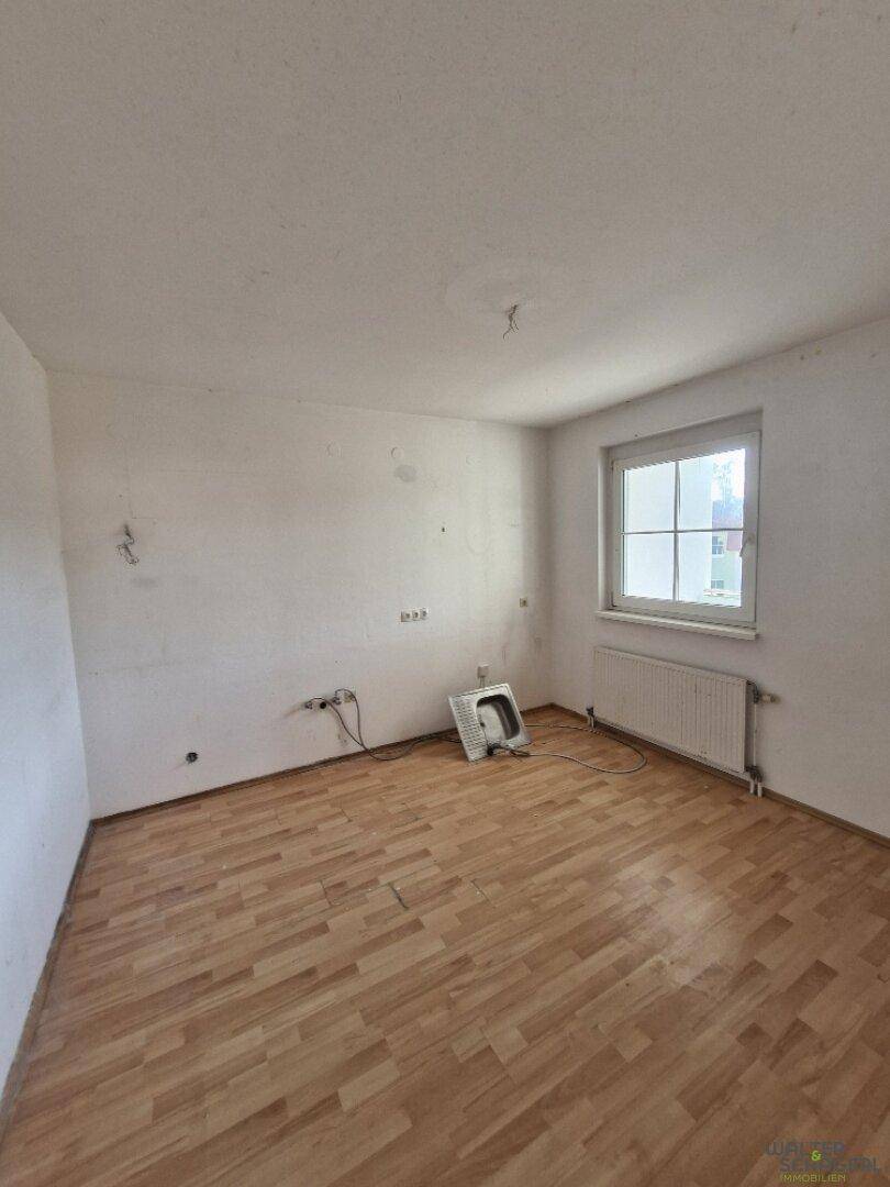Leeres Zimmer mit Holzboden, weißen Wänden und einem Fenster, bereit zur individuellen Gestaltung.