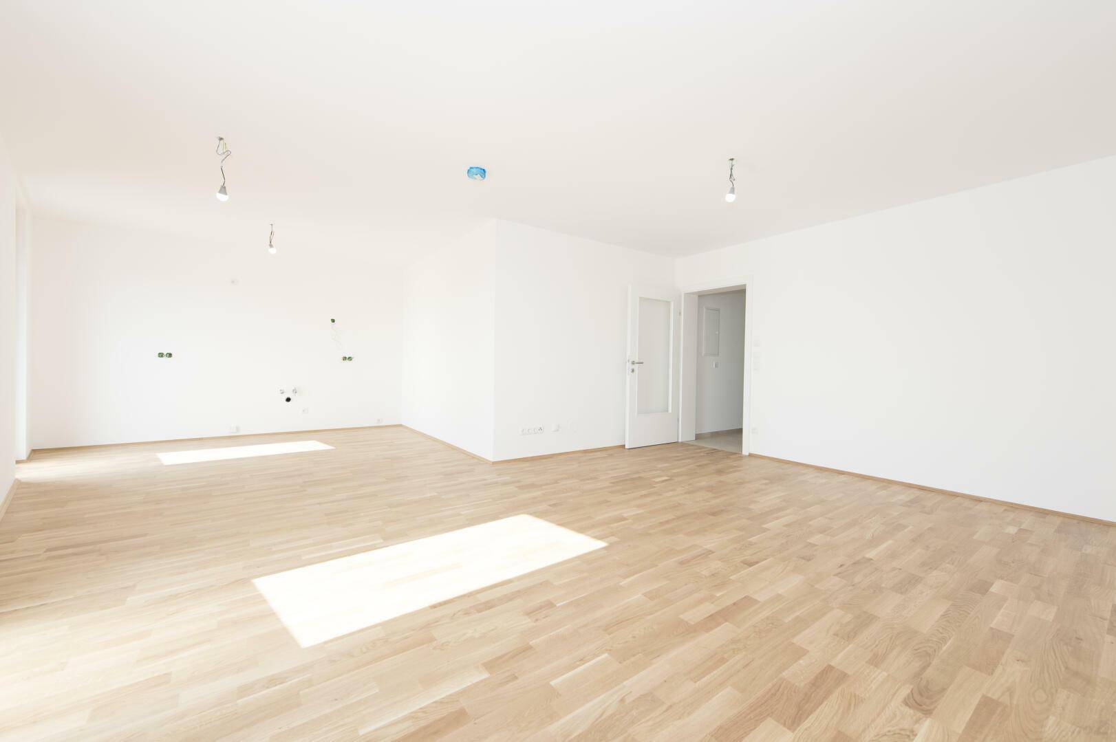 Heller Wohnraum mit Parkettboden, weißen Wänden und vorbereiteten Anschlüssen.