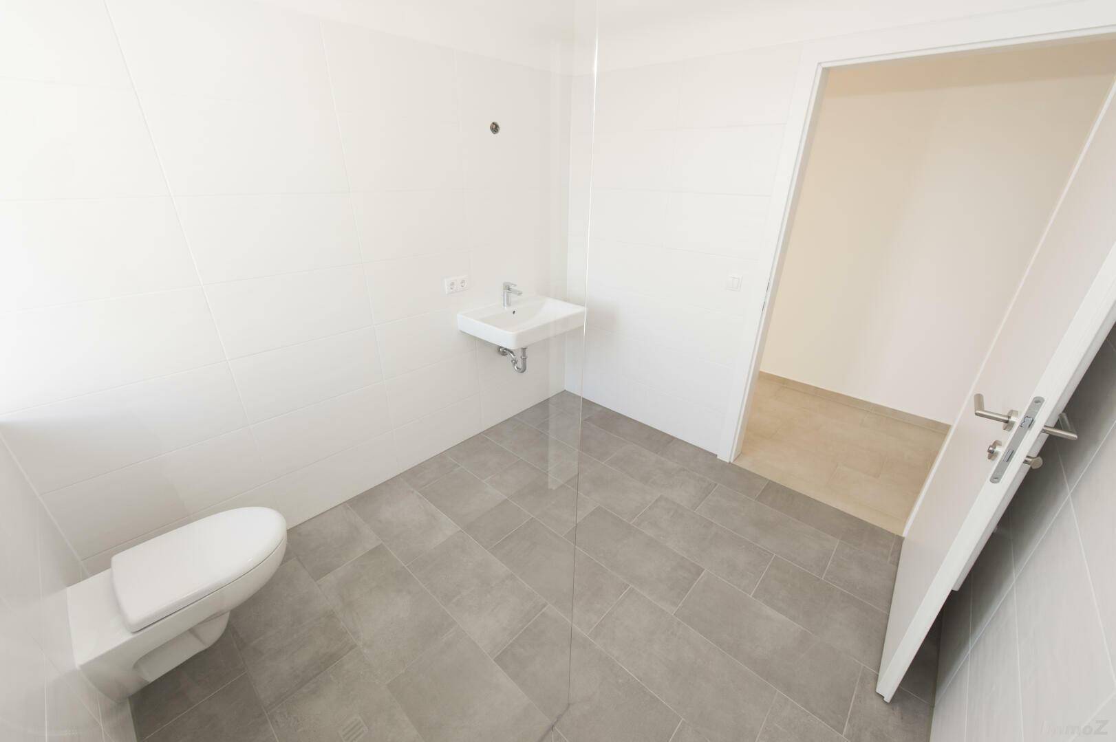 Kleines WC mit wandhängender Toilette und Handwaschbecken auf gefliestem Boden.