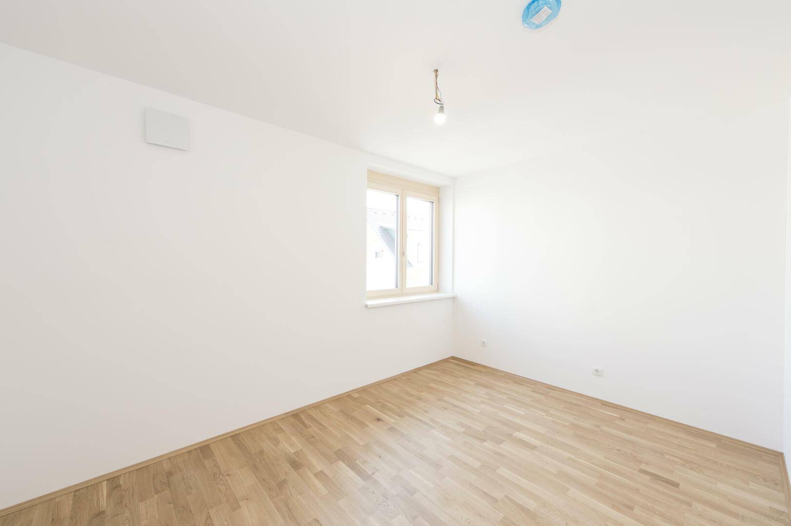 Kleineres Zimmer mit Parkettboden, weißen Wänden und einem Fenster.