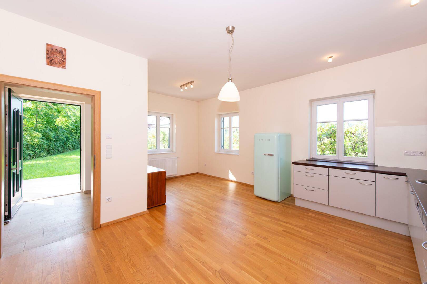 Helle Küche mit Zugang zum Garten, Holzboden und Blick ins Grüne durch die Fenster.