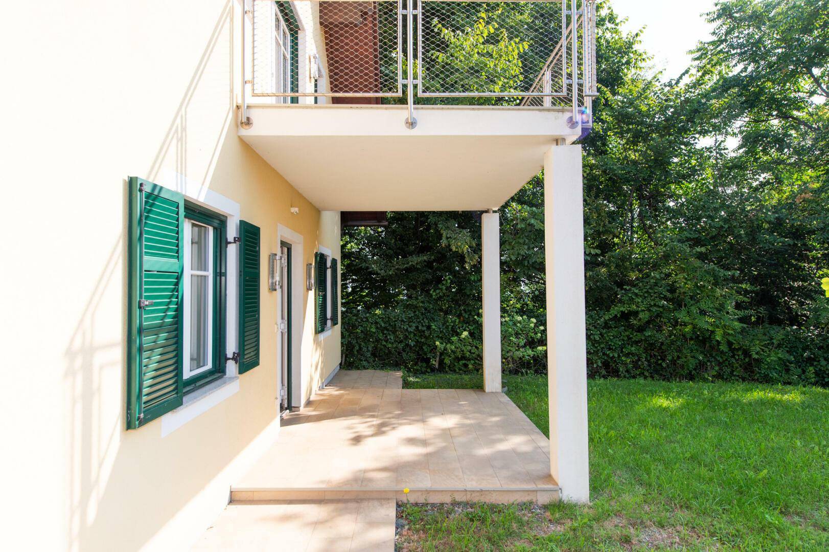 Überdachte Terrasse mit Fliesenboden und Blick ins Grüne, direkt am Haus gelegen.