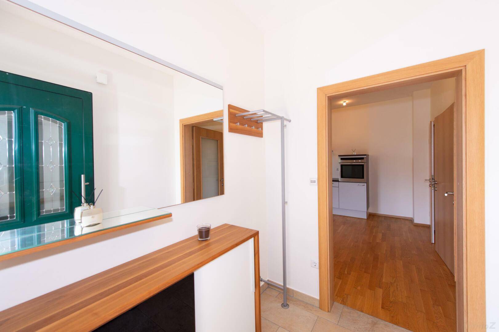 Heller Eingangsbereich mit Fliesenboden, Spiegel und Holzakzenten, führt in weitere Räume.