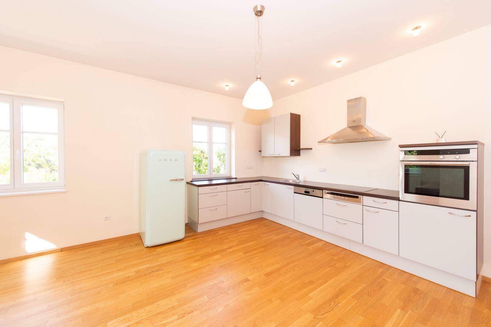 Geräumige Küche mit Holzboden, weißen Schränken und modernen Geräten, viel Tageslicht.