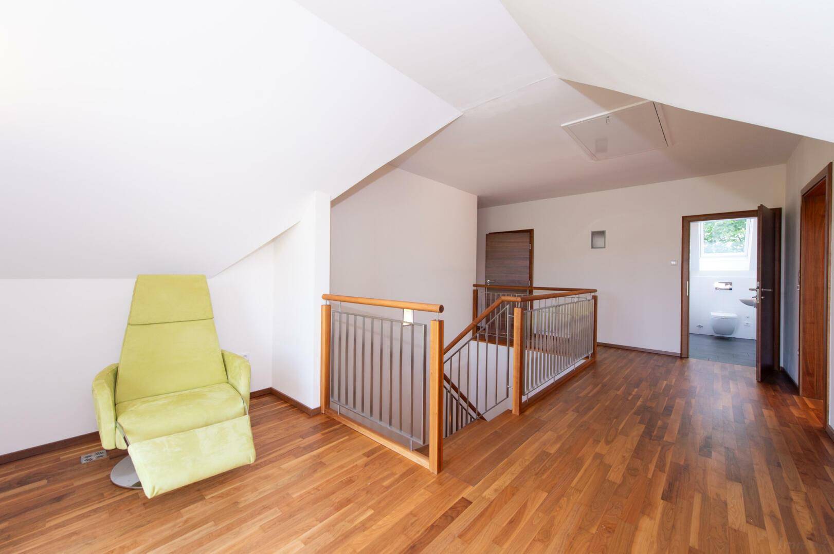 Heller Flur im Dachgeschoss mit Holzboden und Dachschrägen, gemütlicher Sessel.