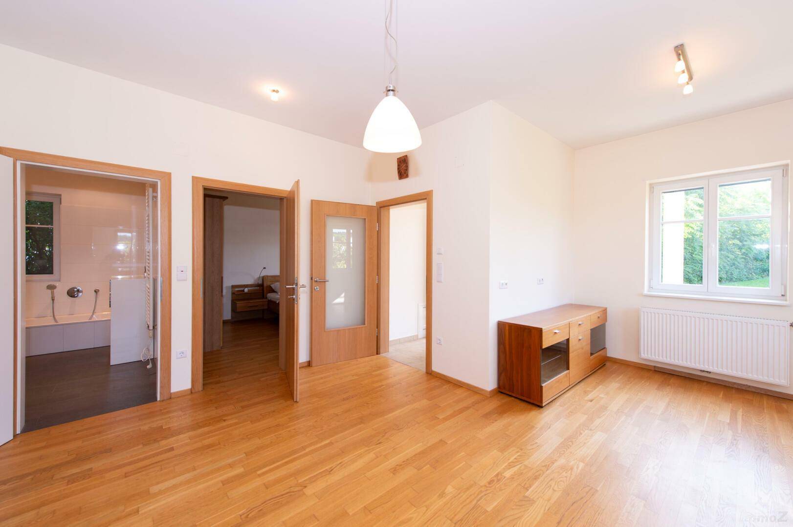 Heller Raum mit Holzboden und mehreren Türen, die zu angrenzenden Zimmern führen.