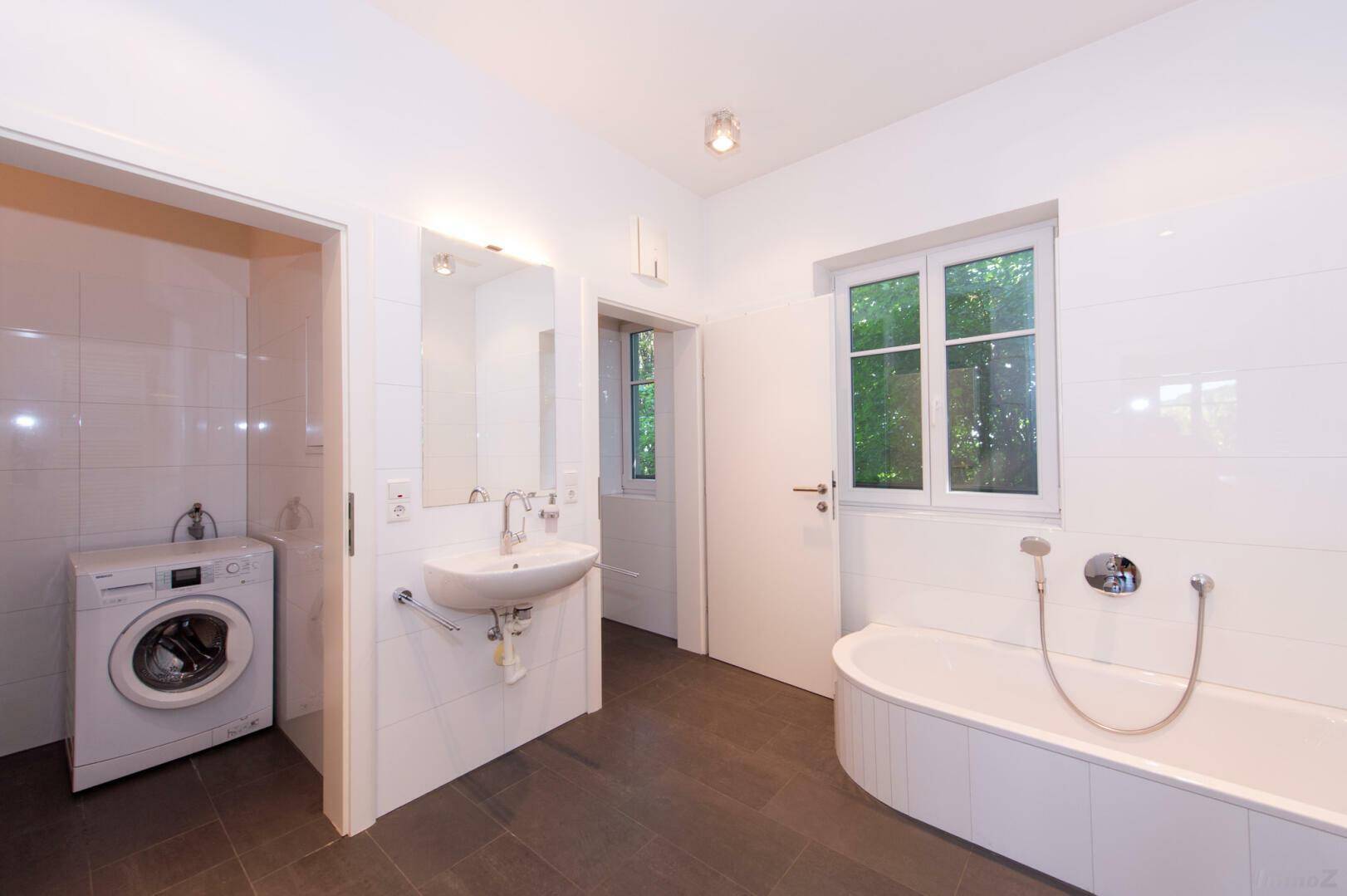 Modernes Badezimmer mit Badewanne, Waschbecken und Waschmaschine, hell gefliest.