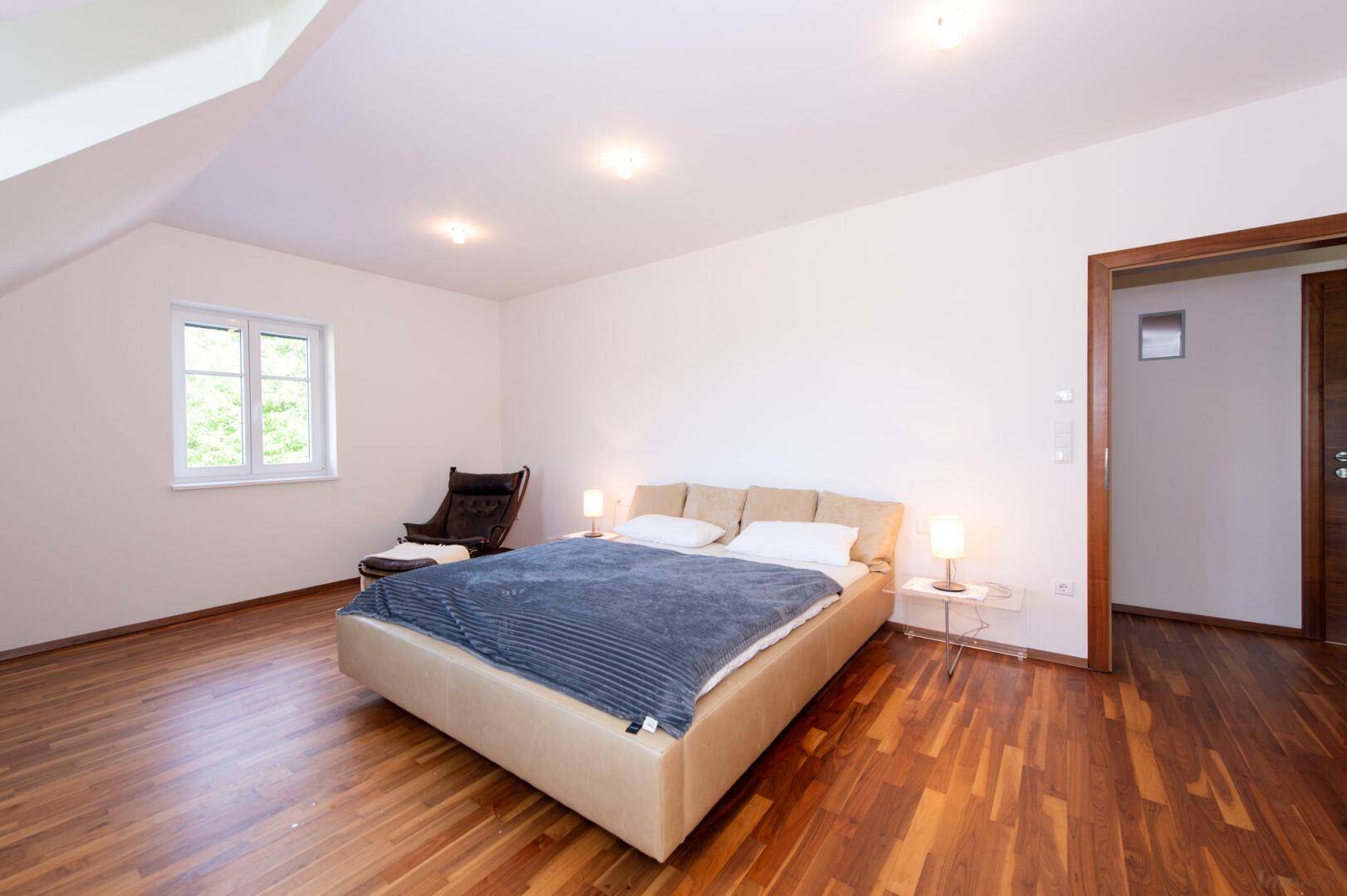 Geräumiges Schlafzimmer im Dachgeschoss mit Doppelbett und Holzboden, viel Tageslicht.