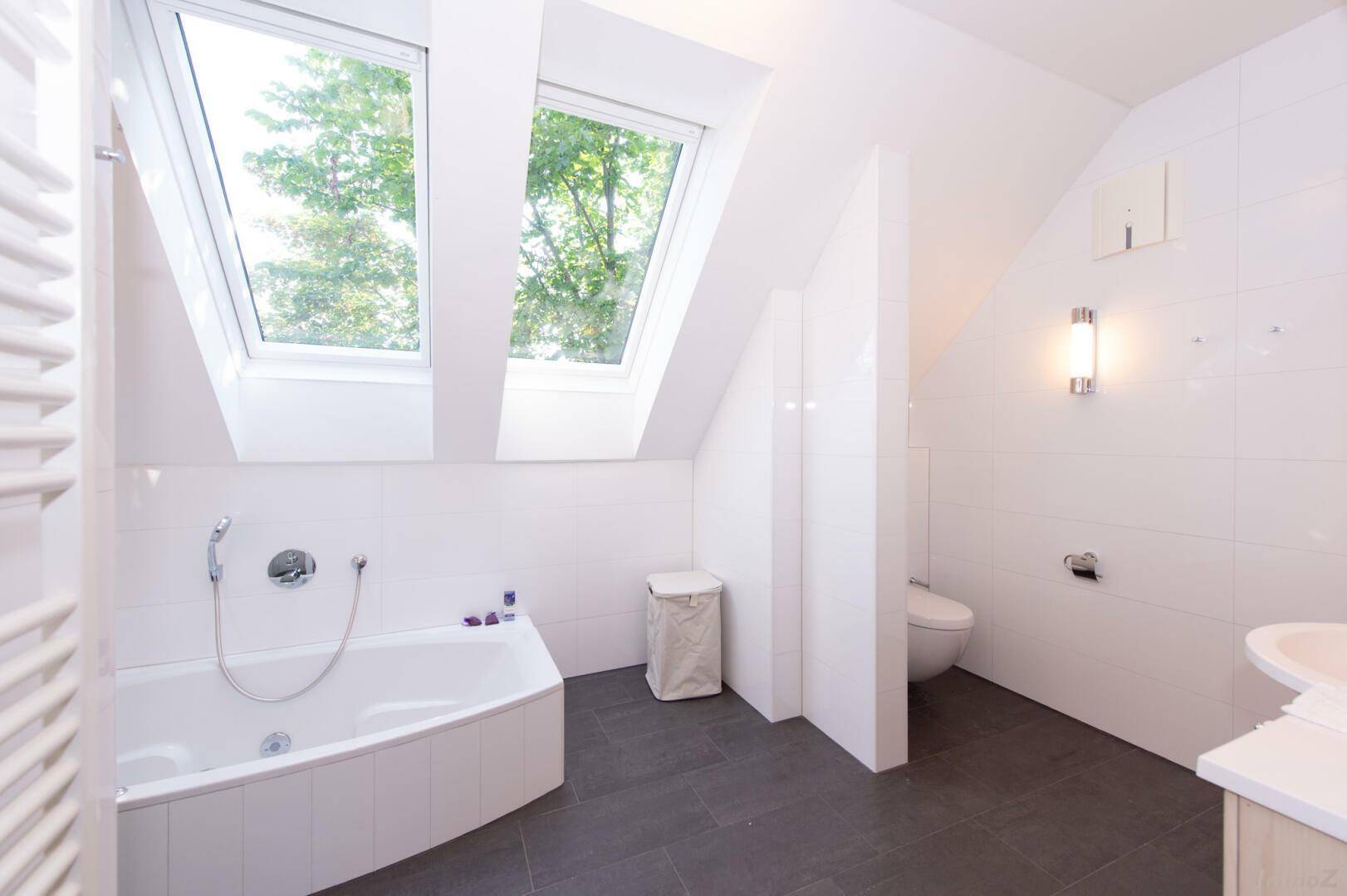 Helles Badezimmer im Dachgeschoss mit Badewanne, Dusche und zwei Dachfenstern.