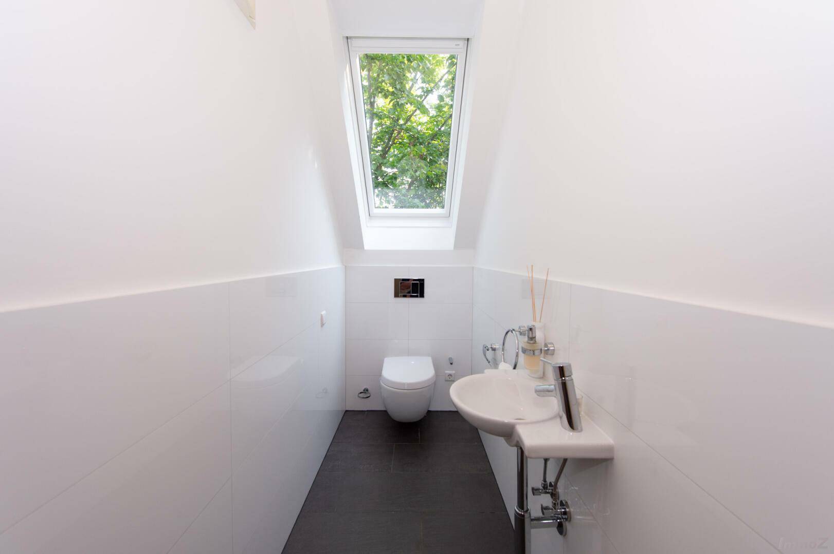 Modernes Gäste-WC mit wandhängendem WC, Waschbecken und Dachfenster für Tageslicht.