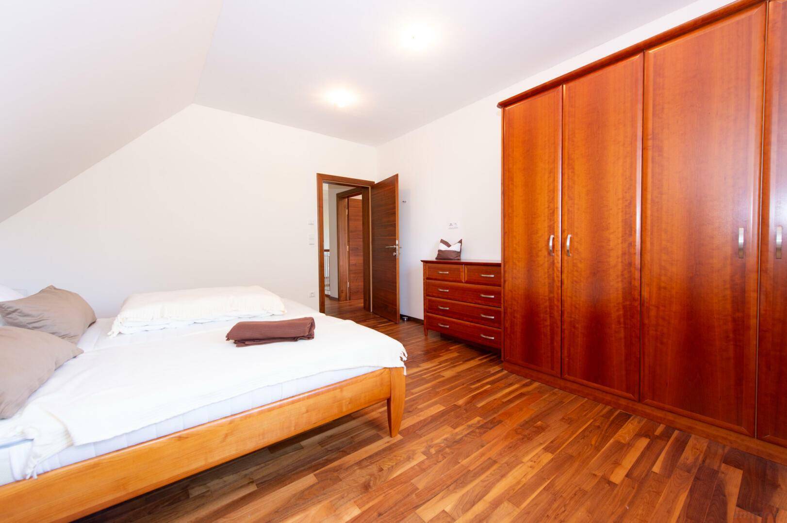 Schlafzimmer im Dachgeschoss mit großem Holzschrank und Holzboden, Zugang zu weiterem Raum.