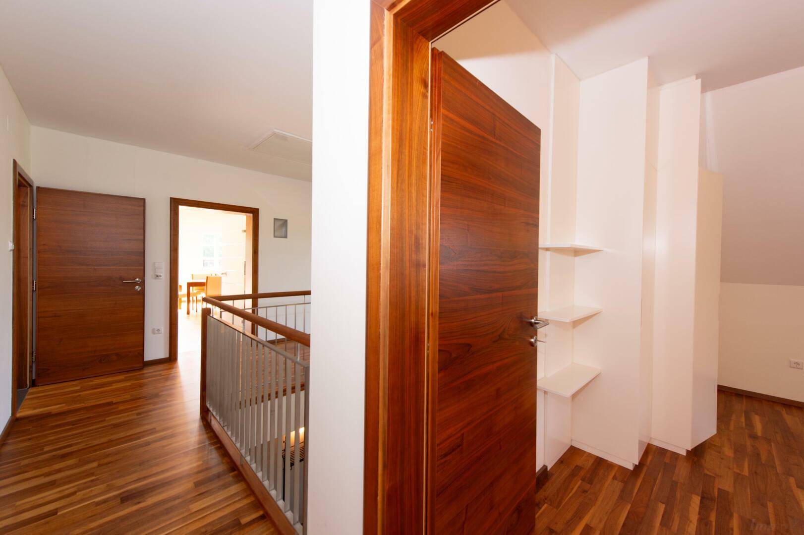 Heller Flur im Dachgeschoss mit Holzboden und Holztreppengeländer, führt zu den Zimmern.