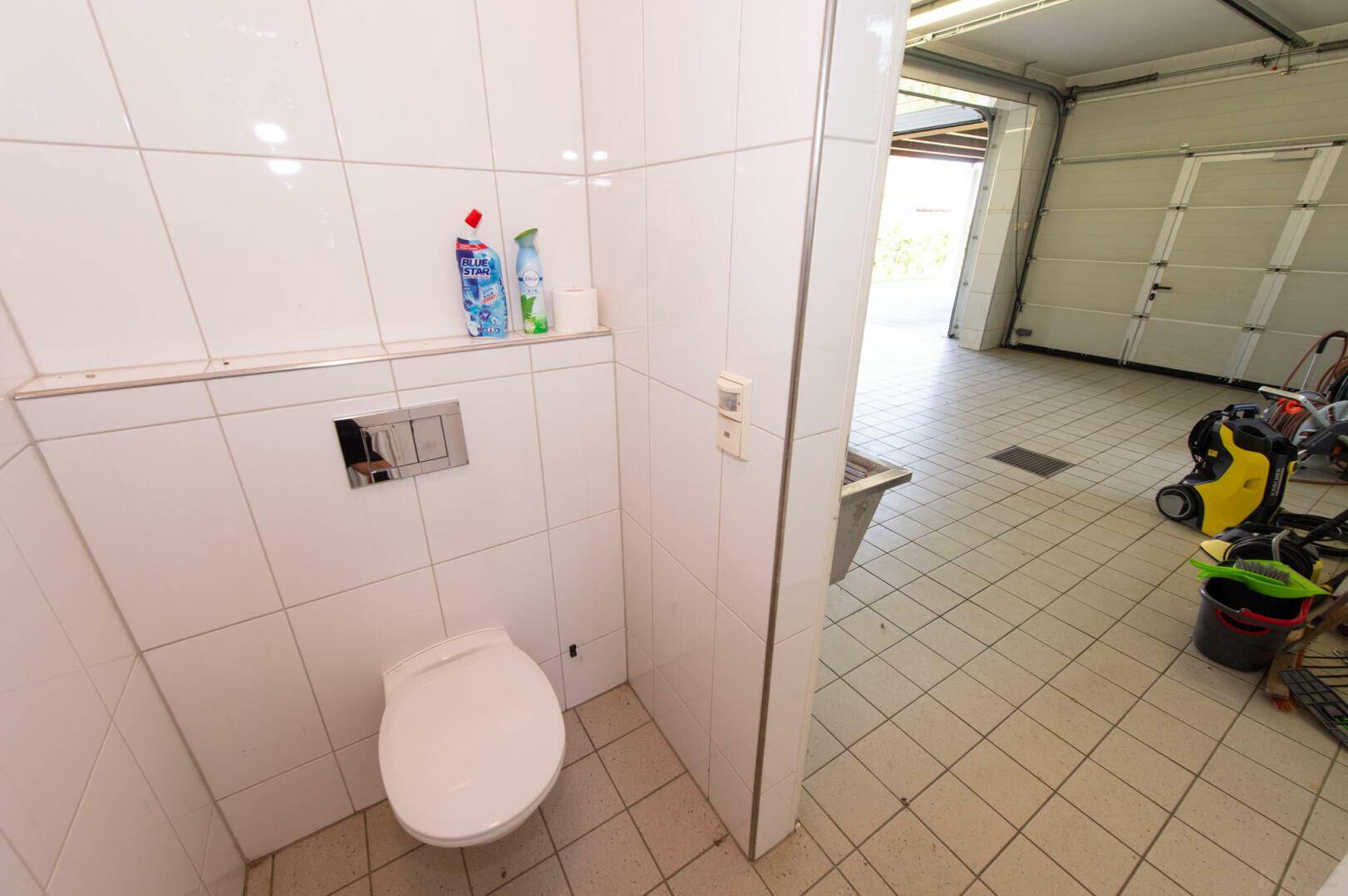 Kleines WC im Garagenbereich mit Fliesen und wandhängender Toilette, funktional.