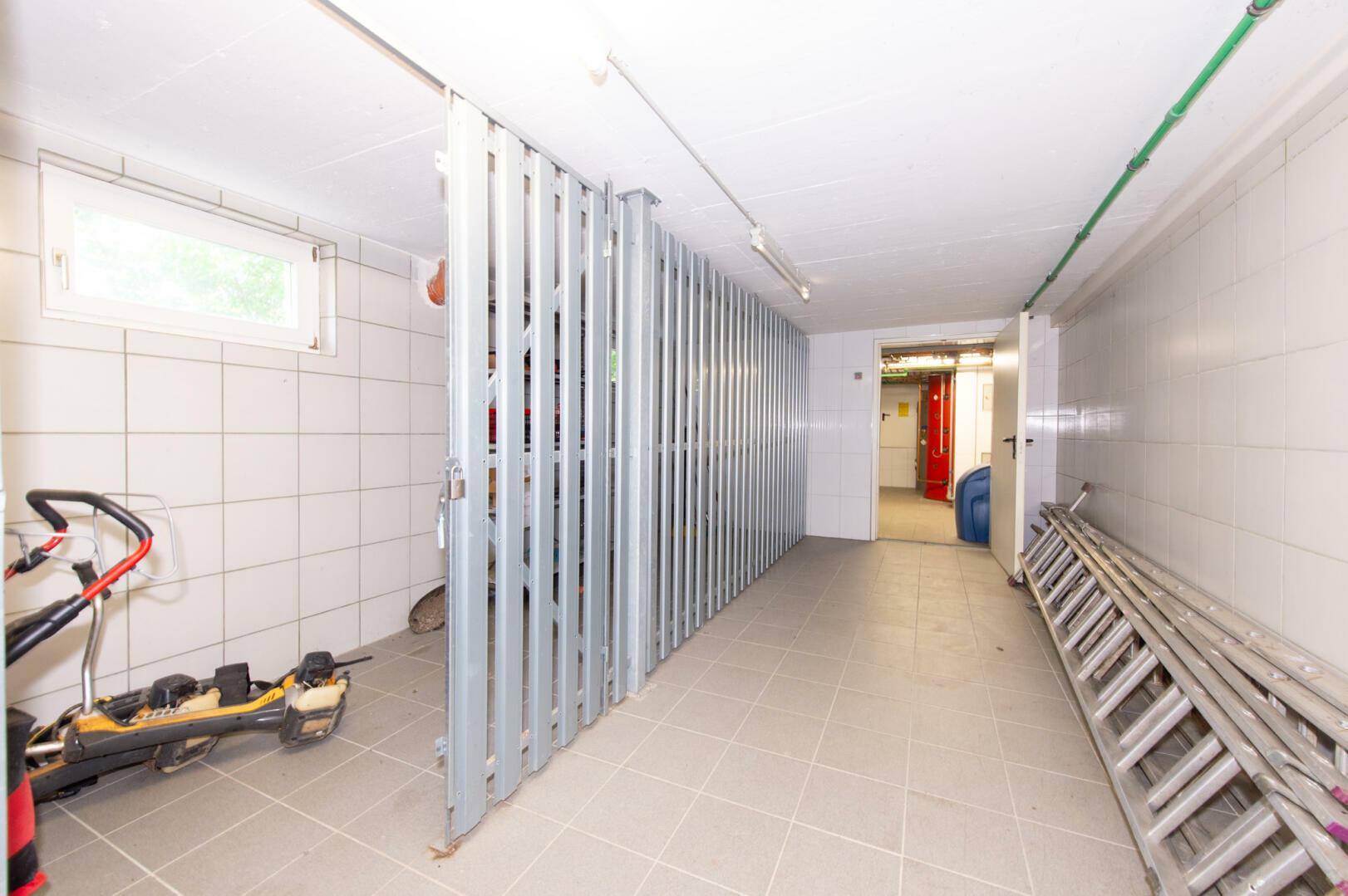 Geräumiger Lagerraum im Keller mit Fliesenboden und Metallabtrennungen, ideal für Stauraum.